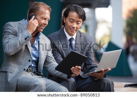 Businessmen using laptop and tablet pc while communication on cell phone
