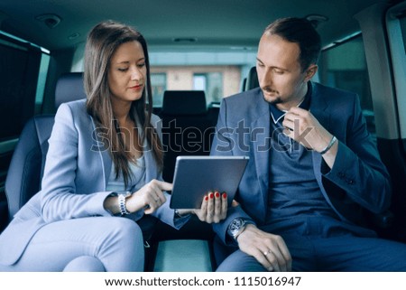 Businessmen and women traveling in VIP car transfer. Women use tablet pc for presentations. The couple inside of modern car watch in a tablet 