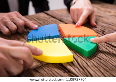 Businesspeople Connecting Pieces Of Multi Colored Pie Chart On Wooden Desk