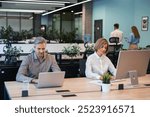 Businesspeople in formalwear working on laptop and PC in the modern office with collegues on the background..