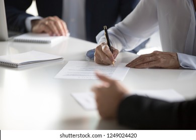 Businesspeople gathered together at business meeting after successful negotiations ready to sign agreement official paper close up focus on businesswoman hands holds pen affirm contract with signature