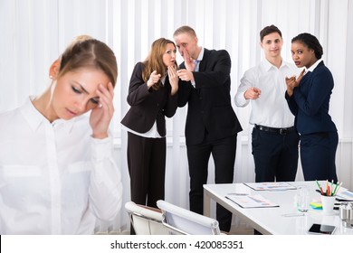 Businesspeople Gossiping Behind Stressed Female Colleague In Office - Shutterstock ID 420085351