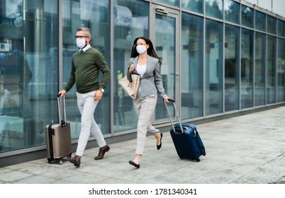Businesspeople with luggage going on business trip, wearing face masks at the airport.