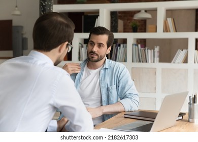 Businesspeople male staff members talking sit at workplace desk. Serious advisor consult client make offer at meeting in office, men colleagues share ideas, discuss new collaborative project concept - Shutterstock ID 2182617303