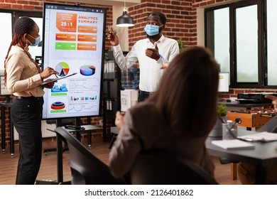 Businesspeople with medical face mask to prevent infection with coronavirus showing business graphs discussing company strategy in startup office. Diverse people working at financial presentation - Powered by Shutterstock