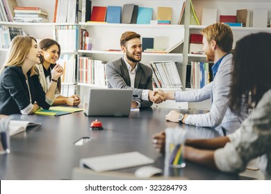 Businesspeople shaking hands in office with coworkers and staff sitting at the table with them