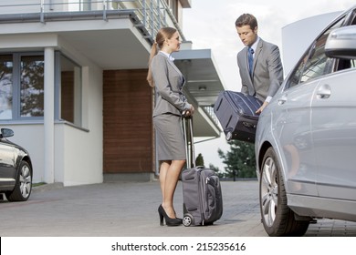 Businesspeople Unloading Luggage From Car Outside Hotel