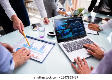 Businesspeople Using Laptop While Analyzing Graphs At Meeting