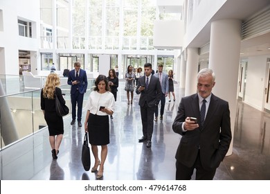 Businesspeople Using Technology In Busy Lobby Area Of Office