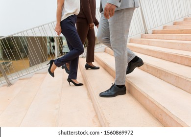 Businesspeople Walking Upstairs And Downstairs. Legs And Feet Of Business Man And Women Wearing Formal Trousers And Shoes. Business Area Concept