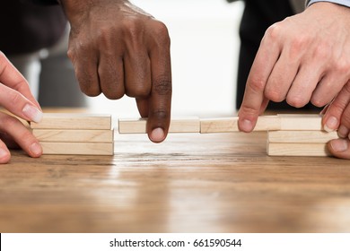 Businesspeople's Hand Holding Wooden Building Blocks To Form A Bridge Over A Gap On Table