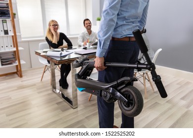 Businessperson Carrying Folded Electric Scooter In Front Of His Colleagues At Office - Shutterstock ID 1522525202
