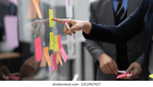 Businessperson teamwork meeting in office and use sticky post notes to brainstorming ideas on glass board. Asian businesswoman planning corporate strategy with colleague for success startup business. - Powered by Shutterstock