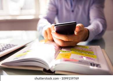 Businessperson Using Mobile Phone With Diary On Desk