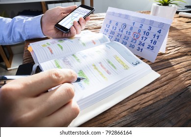 Businessperson's Hand Holding Smartphone With Gantt Chart On Screen While Planning Schedule In Diary - Powered by Shutterstock