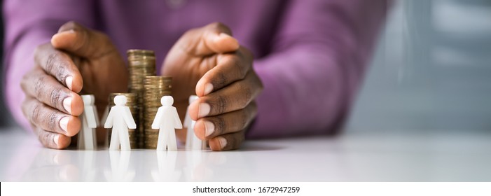 Businessperson's Hand Protecting White Human Figures Surrounding Stacked Golden Coins Over Desk
