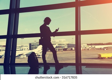 Businesswoman At The Airport. Silhouette Of A Girl With Mobile Phone And Backpack. Business And Travel