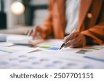 Businesswoman is analyzing financial charts at her desk, using a calculator and a pen to review data and make important business decisions