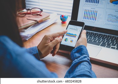 Businesswoman analyzing financial data on smartphone and computer screen.Close up