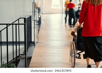 A businesswoman assists her colleague in a wheelchair as they navigate the sleek hallways of a modern startup office, embodying inclusivity and teamwork - Powered by Shutterstock