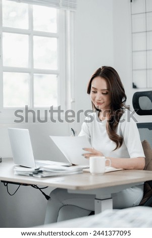 Businesswoman attentively reviewing documents, with a cup of coffee and laptop in her bright, airy home office.