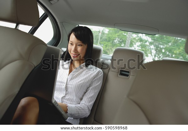 Businesswoman in\
backseat of car using laptop,\
smiling