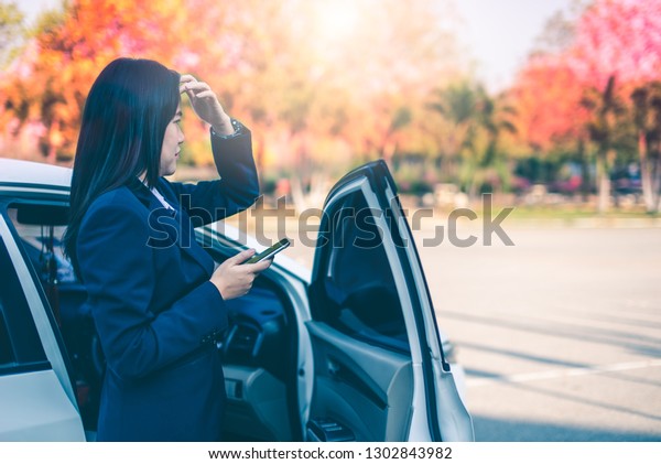 Businesswoman, beautiful\
long hair, parked white car, open the car door and use a mobile\
phone to chat with customer as an appointment near the park with\
colorful trees in\
autumn.