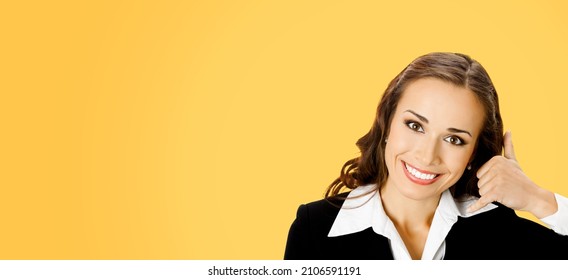 Businesswoman In Black Confident Suit Showing Call Me Hand Sign Gesture, Over Orange Yellow Background. Portrait Of Happy Smiling Gesturing Brunette Woman At Studio. Business Concept Photo. Caller