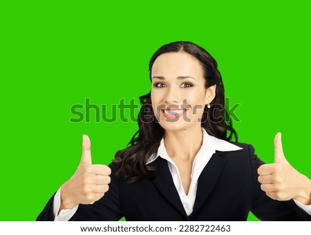 Businesswoman in black confident suit showing thumbs up gesture, isolated on green chroma key chromakey background. Happy smiling gesturing brunette woman. Business concept photo