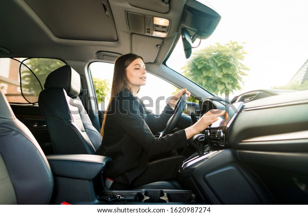 Businesswoman in black suit sits behind the wheel\
of a premium car and looks the way looking at the monitor of\
navigation system