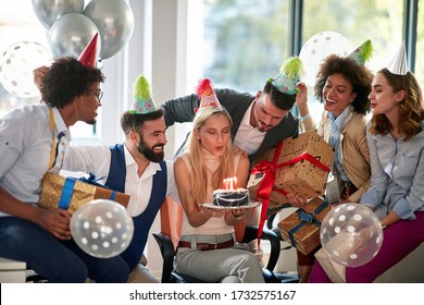 Businesswoman blowing candles on her birthday cake Surpise birthday party in the office. Coworker celebration with decorations.   - Powered by Shutterstock