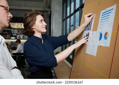 businesswoman and businessman looking at business chart paper on bulletin board in the office - Powered by Shutterstock