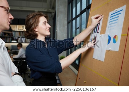 businesswoman and businessman looking at business chart paper on bulletin board in the office