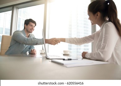Businesswoman and businessman shaking hands over the table with laptop and papers at the office, pleasant business meeting, starting negotiation, conducting job interview
