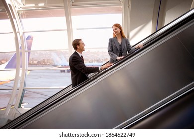 Businesswoman and businessman standing on an escalator and looking at each other on and escalator in the airport