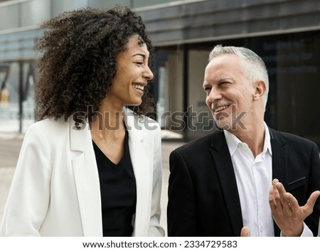 Businesswoman and businessman talking and smiling in the street. Casual meeting between a young executive and a senior ceo having fun outside.