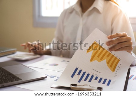 A businesswoman is calculating the financial results of a finance company at the bargraph at the desk to bring the results to her boss.