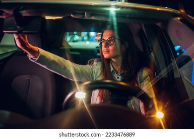 Businesswoman in car driver seat checking rearview window while riding in urban city. Young woman stuck in a traffic while commuting from work at night. Copy space. View trough windshield. - Shutterstock ID 2233476889