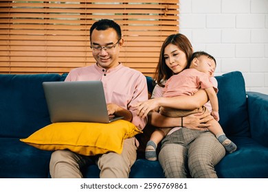Una mujer de negocios lleva a su hija dormida mientras su esposo trabaja diligentemente en una computadora portátil en su oficina en el hogar. Equilibrar el trabajo con la familia y el vínculo con este retrato irradia responsabilidad y amor.
