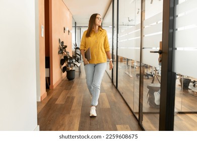 Businesswoman carrying laptop walking through hallway going to leave office after workday, full lengths portrait of cheerful confident freelance woman walking in modern coworking space