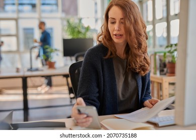 Businesswoman checking her phone while working at her office desk
