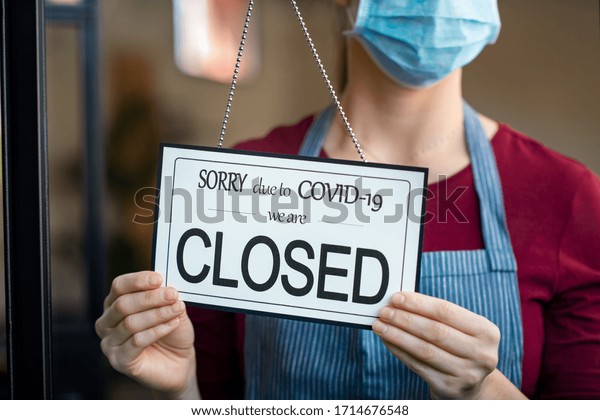 Businesswoman closing her business activity due\
to covid-19 lockdown. Owner with surgical mask close the doors of\
her store due to quarantine coronavirus. Close up sign due to the\
effect of\
COVID-19.
