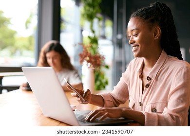 Businesswoman With Coffee Working On Laptop In Cafe Shop Looking At Mobile Phone - Powered by Shutterstock