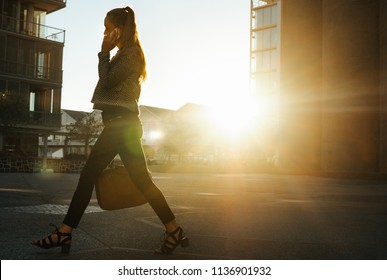 Businesswoman Commuting To Office Early In The Morning Talking Over Mobile Phone. Woman Carrying Handbag Walking On City Street To Office.