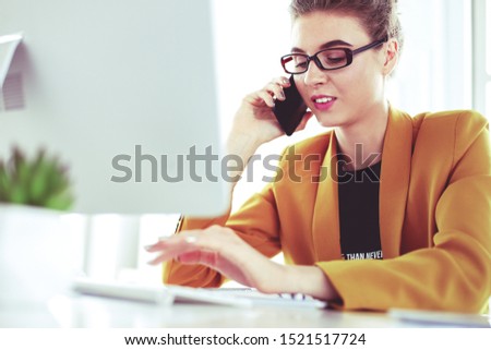 Businesswoman concentrating on work, using computer and cellphone in office