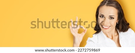 Businesswoman in confident cloth showing ok okay hand sign gesture, over blurred modern office background. Portrait of happy smiling gesturing business woman, isolated orange yellow background.