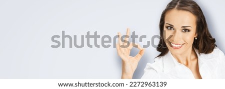Businesswoman in confident cloth showing ok okay hand sign gesture, over blurred modern office background. Portrait of happy smiling gesturing business woman, isolated grey gray background.