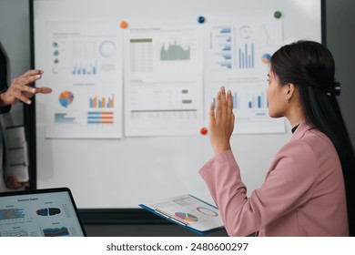 Businesswoman confidently asks a question during a dynamic presentation in an office. The team collaborates on strategies for success, with a modern workspace and diverse colleagues - Powered by Shutterstock