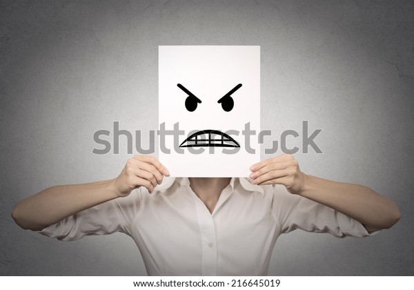 businesswoman covering her face with angry mask\
isolated grey wall background. Negative emotions, feelings,\
expressions, body\
language