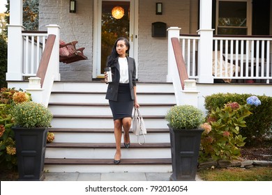 Businesswoman With Cup Of Coffee Leaving Suburban House For Work